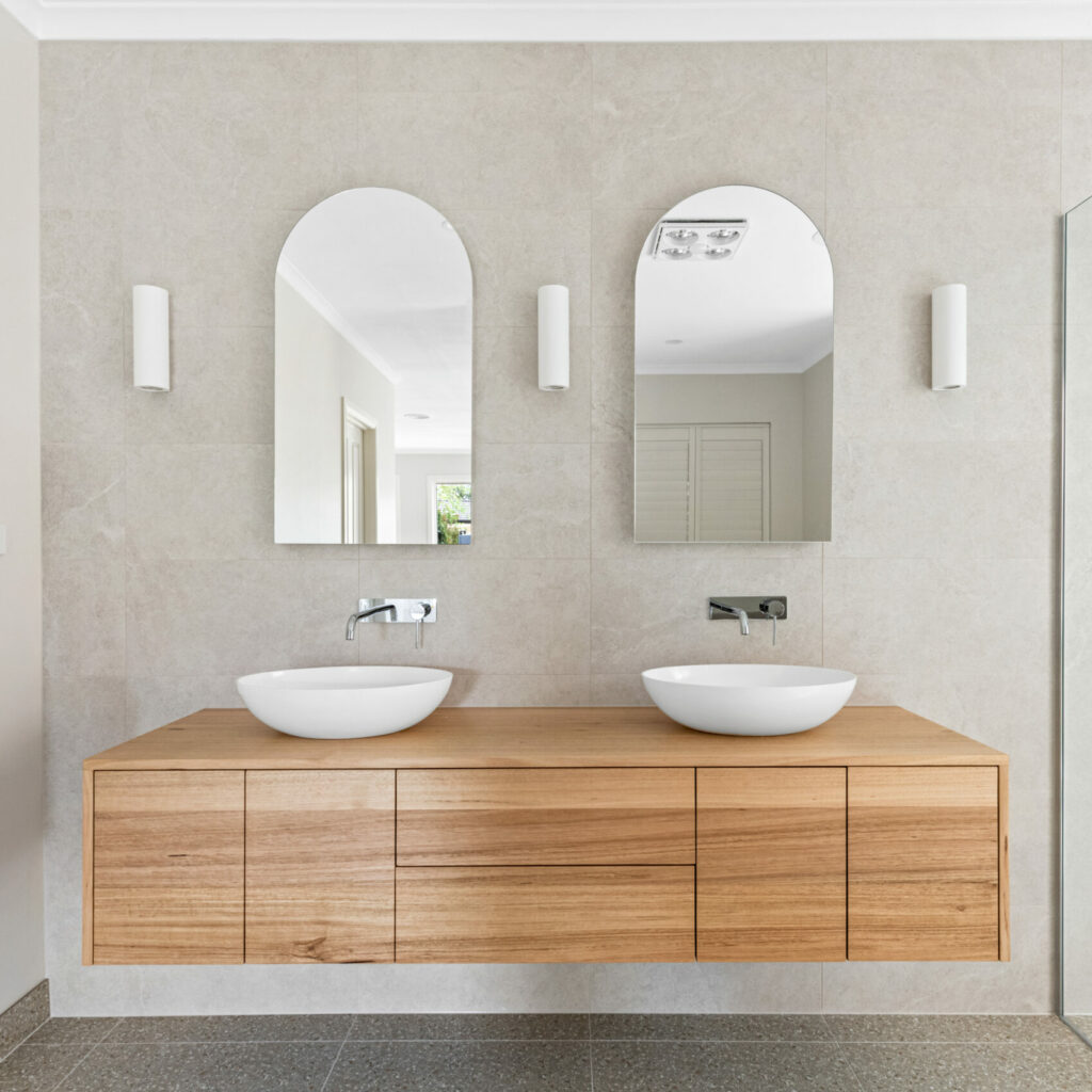 wooden cupboards and draws, light in colour, arched mirrors with white lights either side